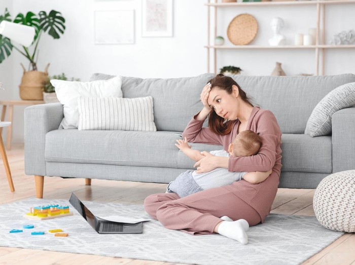 Ilustrasi ibu menyusui sakit kepala Motherhood Exhaustion Concept. Tired young mom breastfeeding baby and working on laptop at home, feeling frustrated, free space