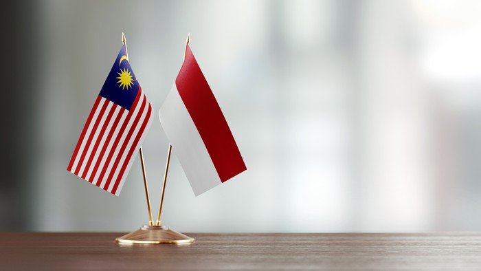 Malaysian and Indonesian flag pair on desk over defocused background. Horizontal composition with copy space and selective focus.