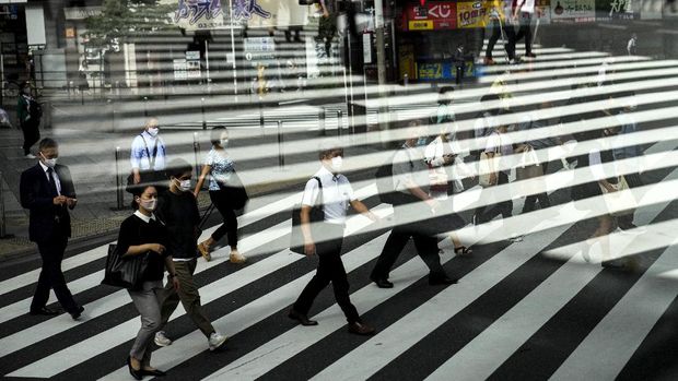 Commuters are reflected in a bus window as they cross the street Thursday, July 15, 2021, in Tokyo. The pandemic-delayed 2020 Summer Olympics open on July 23 without spectators at most venues. (AP Photo/Jae C. Hong)