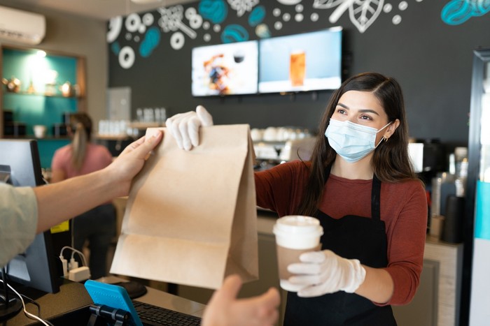 Ilustrasi kafe atau tempat makan Young female staff giving parcel and coffee to customer at takeaway counter in coffee shop