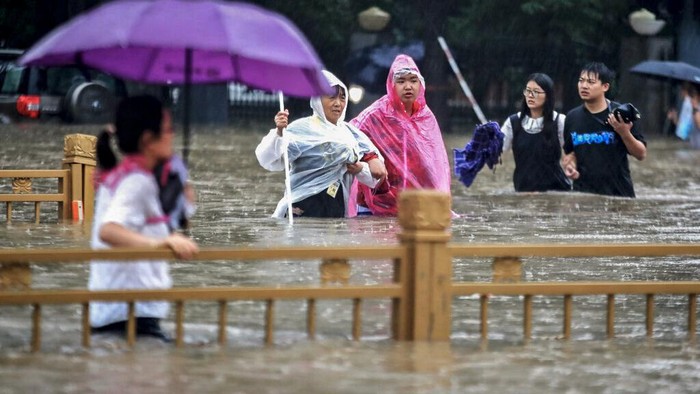Foto: Dahsyatnya Banjir di China People move through flood water after a heavy downpour in Zhengzhou city, central China's Henan province on Tuesday, July 20, 2021. Heavy flooding has hit central China following unusually heavy rains, with the subway system in the city of Zhengzhou inundated with rushing water and thousands of residents having to be relocated. (Chinatopix Via AP)