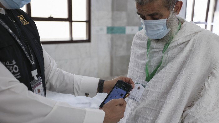 A Saudi member of staff scans a pilgrims hajj card, allowing contactless access to religious sites, accommodation and transport, at a reception centre in Mecca on July 18, 2021. - The plastic cards are available in green, red, yellow or blue with the colour corresponding to markings on the ground guiding pilgrims through the different stages of hajj. Each card contains basic information about each pilgrim including their registration number, exact location of their accommodation, mobile phone number and the ID number of their guide. (Photo by Fayez Nureldine / AFP)