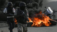 Polisi bersenjata berlindung di dekat ban bekar yang dibakar oleh pengunjuk rasa di Cap-Haitien, Haiti.