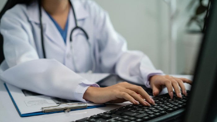 ilustrasi telemedicine Mid adult female doctor reviews patient records on desktop PC