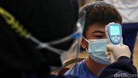 Seorang anak diperiksa suhu tubuh menggunakan thermo gun.