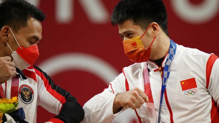 Li Fabin of China , gold medal, right, celebrates on the podium with silver medal Eco Yuli Irawan of Indonesia in the mens 61kg weightlifting event, at the 2020 Summer Olympics, Sunday, July 25, 2021, in Tokyo, Japan. (AP Photo/Luca Bruno)