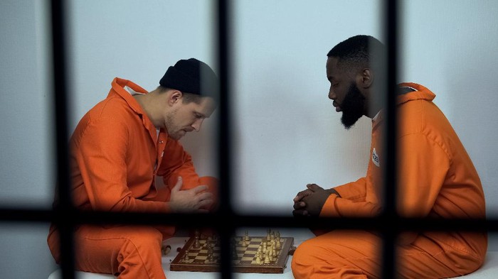 African american and caucasian criminals playing chess in cell, hobby in prison