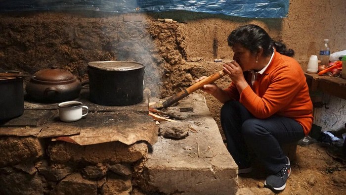 The future first lady of Peru, Lilia Paredes, 48, blows air through a hollow reed to get a fire going in her wood-burning stove in her adobe home in the rural hamlet of Chugur, Peru, Thursday, July 22, 2021. Her husband, leftist Pedro Castillo catapulted from unknown to president-elect with the support of the country's poor and rural citizens, many of whom identify with the struggles the teacher has faced. (AP Photo/Franklin Briceno)