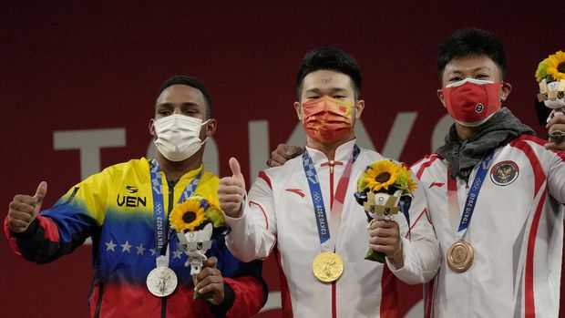 Gold medalist Shi Zhiyong of China, center, is flanked by silver medalist Julio Ruben Mayora Pernia of Venezuela, left, and bronze medalist Rhamat Erwin Abdullah of Indonesia on the podium of the men's 73kg weightlifting event, at the 2020 Summer Olympics, Wednesday, July 28, 2021, in Tokyo, Japan. (AP Photo/Luca Bruno)