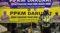 Seorang Polisi berdiri di depan baliho pengumuman pelaksanaan Pemberlakuan Pembatasan Kegiatan Masyarakat (PPKM) Darurat di Jalan Raya Bogor, Jakarta.  