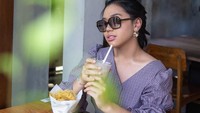 Menikmati minuman dingin sambil menyantap camilan memang jadi momen santai paling asyik. Mengenakan outfit ungu, Aminda duduk di kafe kekinian.  Foto: instagram @amindanac