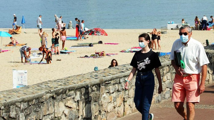 People wearing face masks to protect against coronavirus walk on the pedestrian promenade along the beach in Biarritz, southwestern France, Wednesday, July 28, 2021. Local authorities in France are re-imposing mask mandates and other virus restrictions because of fast-growing infections with the delta variant, which is causing COVID-19 hospitalizations in France to rise again. (AP Photo/Bob Edme)