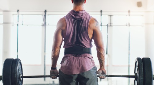 Rearview shot of a muscular man lifting a barbell in a gym