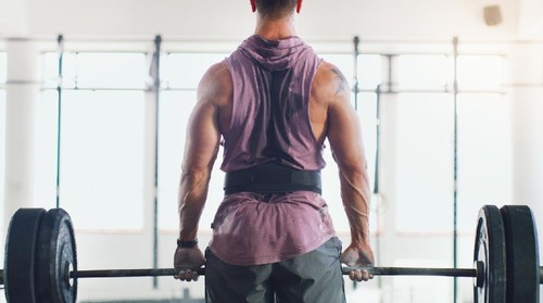 Rearview shot of a muscular man lifting a barbell in a gym