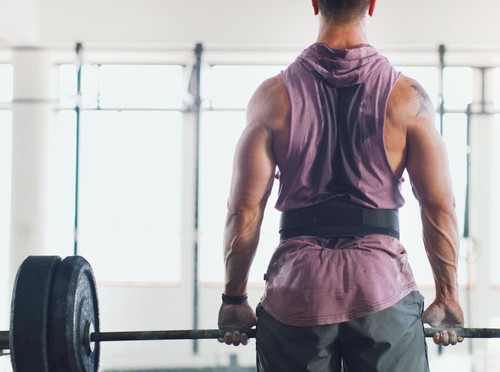 Rearview shot of a muscular man lifting a barbell in a gym