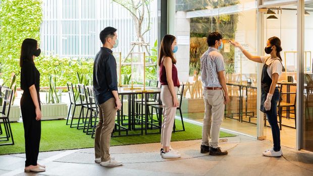 Ilustrasi restoran saat pandemi Asian waitress wear protective face mask scan customer temperature by thermometer before entering the restaurant to protect infection from coronavirus covid-19, social distancing concept
