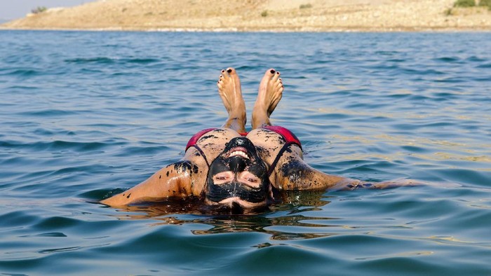 A woman floating on her back in the Dead Sea after coating herself in mineral-rich mud