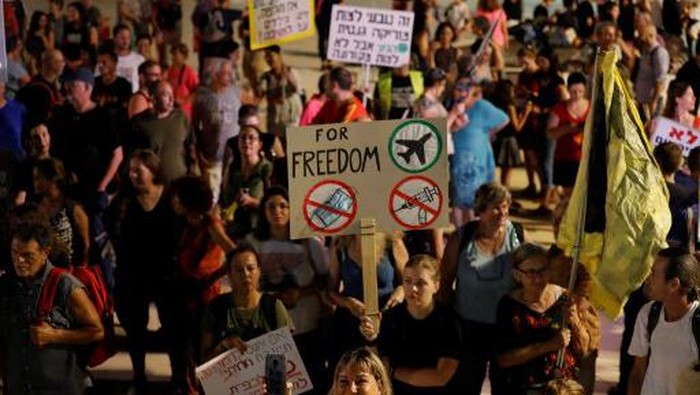 Israelis lift placards at a rally denouncing the governments renewed restrictions to combat COVID-19, in the central coastal city of Tel Aviv, on July 31, 2021. - Israel was quick to roll out its vaccination campaign and had dropped many restrictions on public gatherings in June, as new COVID-19 cases shrank from 10,000 a day to less than 100. But infections have soared in recent weeks, and masks are once again mandatory in enclosed public places, leading to the announcement on July 29 of the start of a vaccine booster campaign for over 60s, as concern mounts over the fast-spreading Delta variant of the coronavirus. (Photo by Ahmad GHARABLI / AFP)