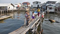 Warga berjalan di atas jembatan kayu di perkampungan nelayan Muara Angke, Jakarta Utara, Sabtu (31/7/2021). Ancaman tenggelamnya Jakarta kembali menjadi sorotan usai disinggung Presiden Amerika Serikat Joe Biden. Pernyataan soal Indonesia itu disampaikan Biden saat mengunjungi kantor Direktur Intelijen Nasional.