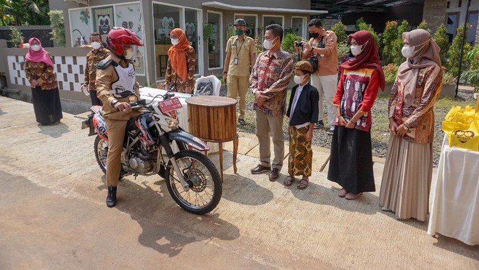 Bupati Batang Wihaji (tengah) mengendarai sepeda motor menghadiri acara khitan dengan sistem drive thru di Desa Tambahrejo, Bandar, Kabupaten Batang, Jawa Tengah, Selasa (3/8/2021). Pemerintah setempat mengizinkan warga Kabupaten Batang mengadakan acara hajatan secara drive thru atau sistem layanan tanpa turun saat pandemi COVID-19 untuk mengurangi laju penyebaran virus COVID-19. ANTARA FOTO/Harviyan Perdana Putra/rwa.