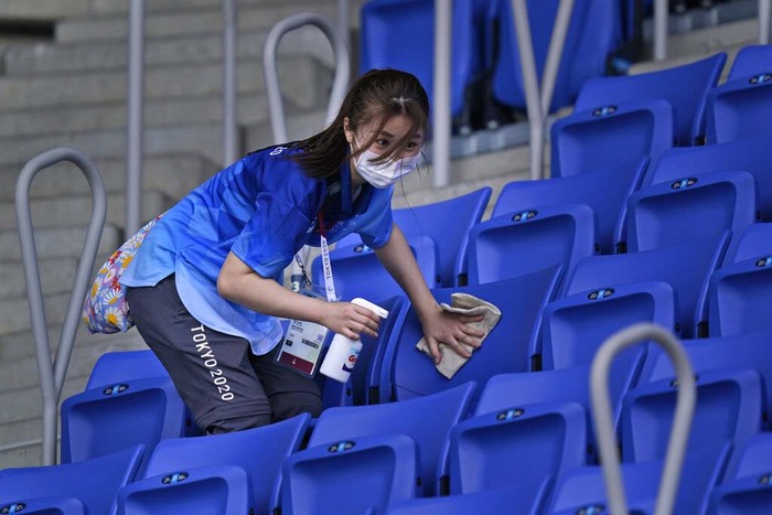 A volunteer cleans seats meant for spectators at the Ariake Tennis Center ahead of the 2020 Summer Olympics, Friday, July 23, 2021, in Tokyo, Japan. (AP Photo/Seth Wenig)