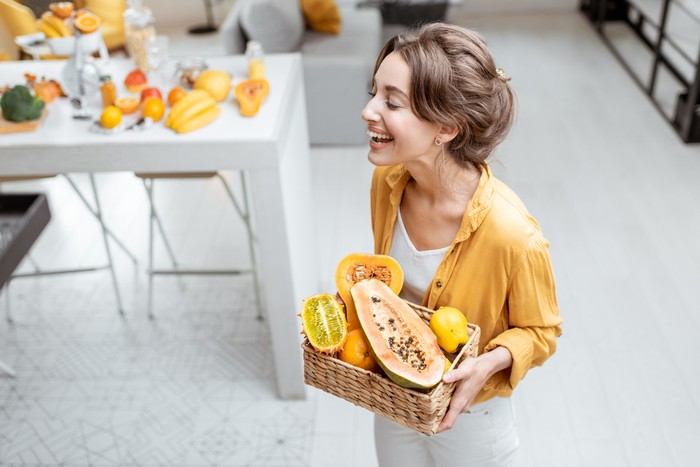 Ilustrasi pepaya Portrait of a young and cheerful woman with exotic fruits at home. Concept of wellbeing, healthy food and homeliness