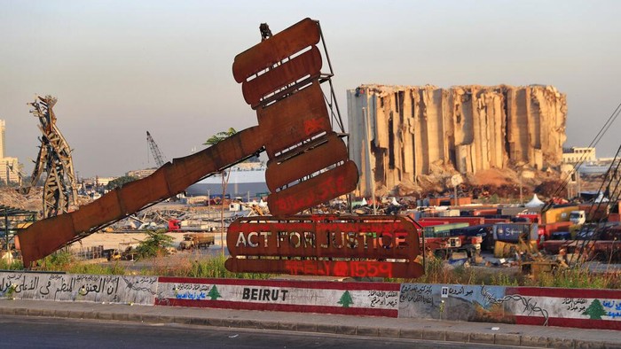 A justice symbol monument is seen in front of towering grain silos that were gutted in the massive August 2020 explosion at the port that claimed the lives of more than 200 people, in Beirut, Lebanon, Wednesday, Aug. 4, 2021. A year after the deadly blast, families of the victims are consumed with winning justice for their loved ones and punishing Lebanon's political elite, blamed for causing the disaster through their corruption and neglect. (AP Photo/Hussein Malla)
