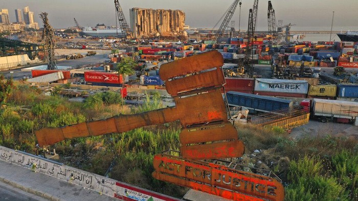 A justice symbol monument is seen in front of towering grain silos that were gutted in the massive August 2020 explosion at the port that claimed the lives of more than 200 people, in Beirut, Lebanon, Wednesday, Aug. 4, 2021. A year after the deadly blast, families of the victims are consumed with winning justice for their loved ones and punishing Lebanon's political elite, blamed for causing the disaster through their corruption and neglect. (AP Photo/Hussein Malla)