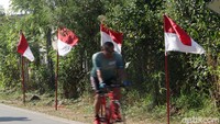 Seorang pesepeda melintas di depan deretan bendera merah putih.
