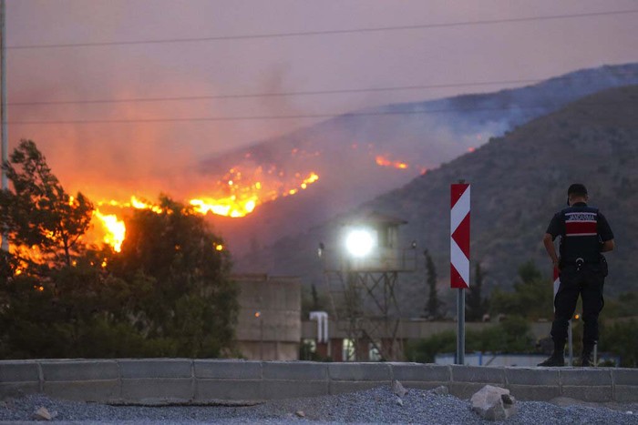 People stand in front of Kemerkoy Thermal Power Plant with the blaze approaching in the background, in Milas, Mugla, Turkey, Tuesday, Aug. 3, 2021. Turkish President Recep Tayyip Erdogan’s government is facing increased criticism over its apparent poor response and inadequate preparedness for large-scale wildfires that have left eight people dead and forced thousands to flee their homes. (AP Photo/Emre Tazegul)