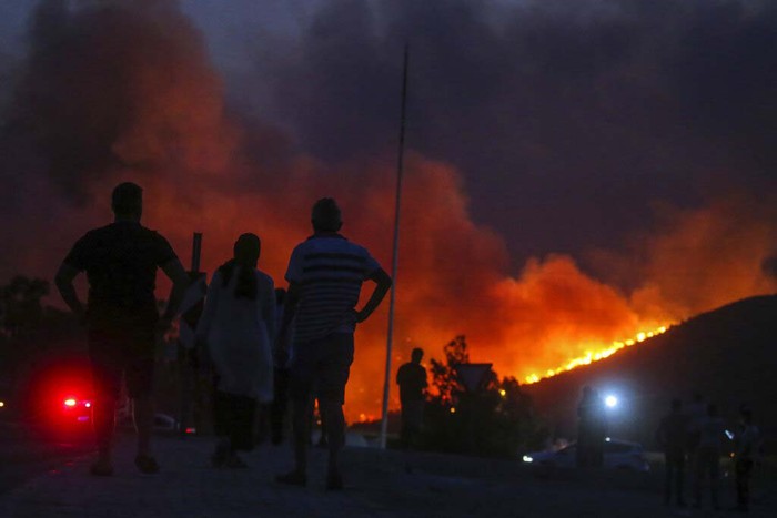 People stand in front of Kemerkoy Thermal Power Plant with the blaze approaching in the background, in Milas, Mugla, Turkey, Tuesday, Aug. 3, 2021. Turkish President Recep Tayyip Erdogan’s government is facing increased criticism over its apparent poor response and inadequate preparedness for large-scale wildfires that have left eight people dead and forced thousands to flee their homes. (AP Photo/Emre Tazegul)