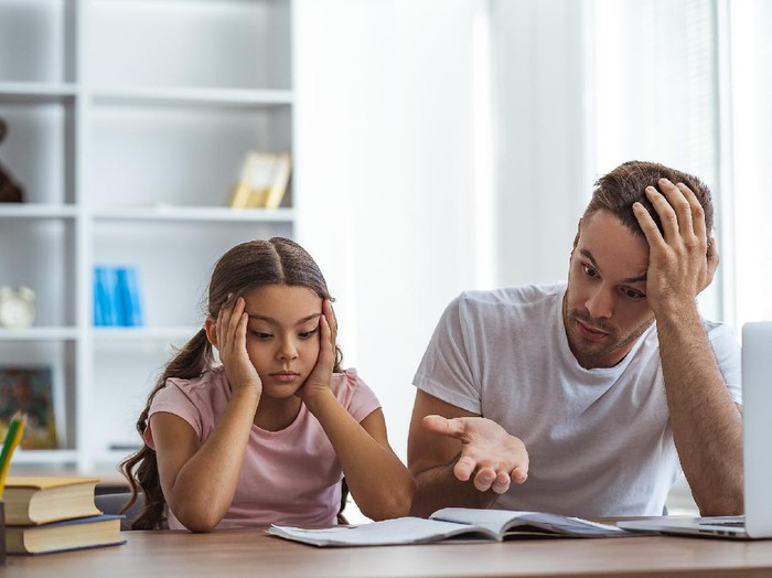 1266903255 Little girl feeling sad while online learning and homeschooling with her mother.