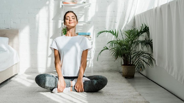 beautiful happy girl with closed eyes practicing yoga in lotus position in bedroom in the morning