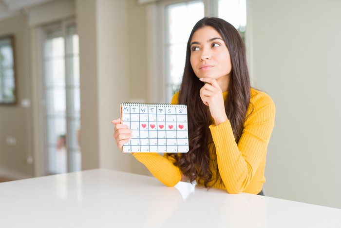 Young woman holding menstruation calendar serious face thinking about question, very confused idea