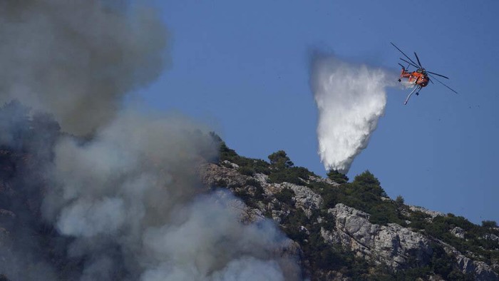 Melihat Proses Pemadaman Kebakaran Hutan di Yunani A firefighting helicopter pours water onto a wildfire in northern Athens, Saturday, Aug. 7, 2021. Wildfires rampaged through Greek forests for yet another day Saturday, threatening homes and triggering more evacuations a day after hundreds of people were plucked off beaches by ferries in a dramatic overnight rescue. (AP Photo/Lefteris Pitarakis)