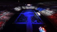 Awalnya, lampu stadion dimatikan secara menyeluruh sehingga memperlihatkan lampu-lampu dari telepon genggam para atlet di tengah lapangan. Getty Images/Rob Carr 