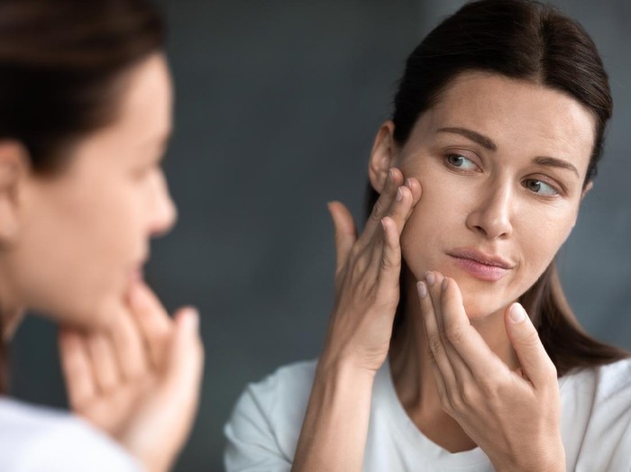 Ilustrasi Skincare Happy woman doing routine skin care at home with beauty products. Woman sitting on bed at home and applying face cream.