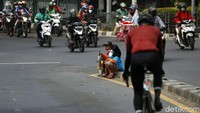 Dua orang anak menunggu mobil yang berhenti saat lampu menyala merah sambil duduk di pembatas jalan.