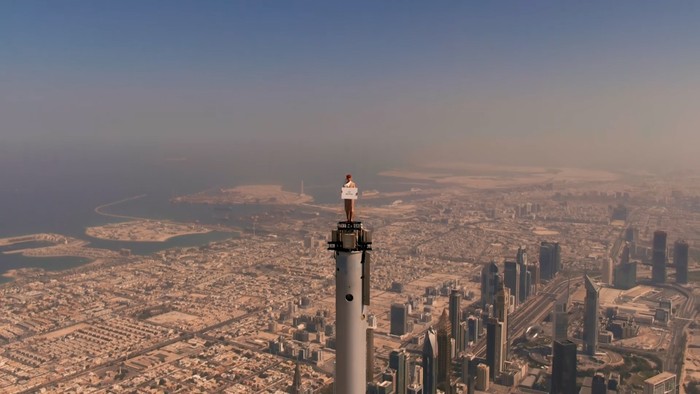 Pramugari Emirates Seorang pramugari dengan tersenyum menunjukkan lembaran kertas dengan tulisan ajakan untuk terbang dengan maskapai Emirates. Tak main-main, dia berdiri di puncak menara Burj Khalifa.