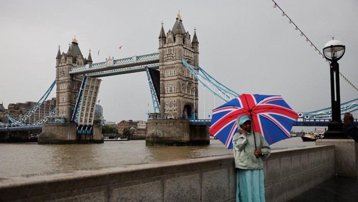 A pedestrian poses for a picture  by Tower Bridge as it is stuck in an open position due to a technical fault, in central London on August 9, 2021. - Londons iconic Tower Bridge remained closed to traffic on August 9 after suffering a technical fault, resulting in it being unable to close. (Photo by Tolga Akmen / AFP)
