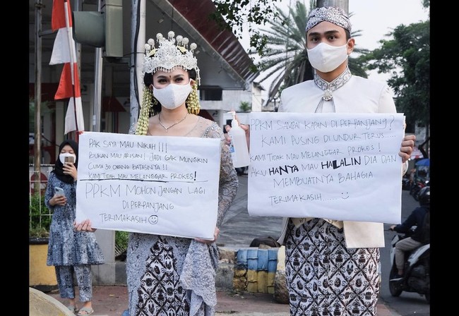 Bergaya bak pengantin mereka berpose di pinggir jalan sambil membawa karton seperti orang yang berdemo. Pak saya mau nikah!!! Bukan mau arisan! Jadi gak mungkin cuma 30 orang batasnya!! Kami tidak akan melanggar prokes! PPKM mohon jangan lagi diperpanjang. Terimakasih, demikian yang tertulis di karton yang dibawa oleh Nadya.Foto: Dok. Instagram @lutfiagizal.