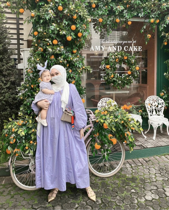 Saat keluar rumah, Dian Pelangi mengenakan dress lilac dan hijab pashmina putih. Ia berpose sambil menggendong Rumi yang memakai dres dan headband. Foto: Dok. Instagram @dianpelangi.