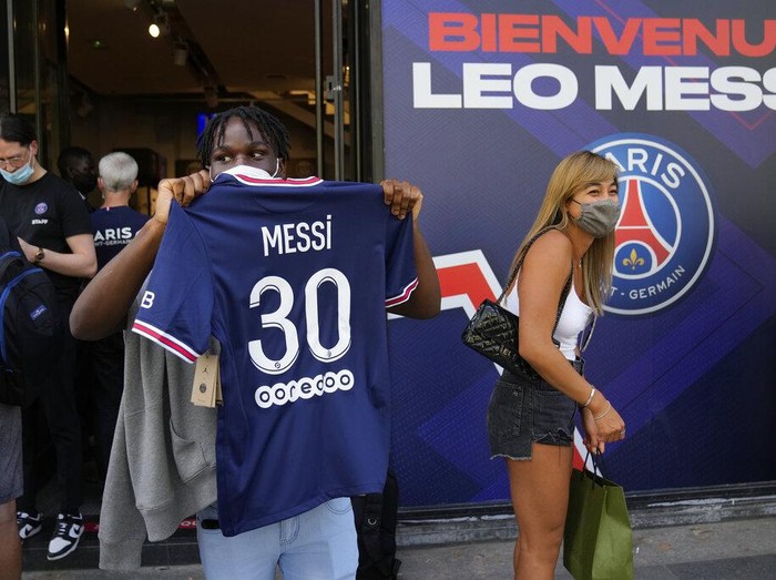 A Parsi Saint-Germain supporter shows a jersey bearing the name of Lionel Messi he just bought as Scarlett Su, right, from New York, smiles outside the official PSG shop, Wednesday, Aug. 11, 2021 in Paris. Lionel Messi is a 
