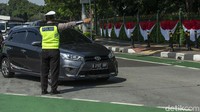 Petugas mengamati pergerakan kendaraan roda empat yang melintas. Kendaraan yang berpelat ganjil akan diberhentikan.