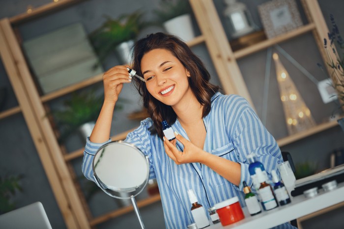 Ilustrasi Skincare Young woman applying serum on her face while looking at mirror..