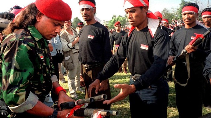 Commander of the pro-Indonesia Aitarak militia, Eurico Guterres (L) receives guns from miltiamen during a ceremony at a sports field in Dili 19 August 1999. Nearly two hundred assorted firearms, mostly homemade, were handed over to the Indonesian police in the presence of UN witnesses. AFP PHOTO (Photo by WEDA / AFP)