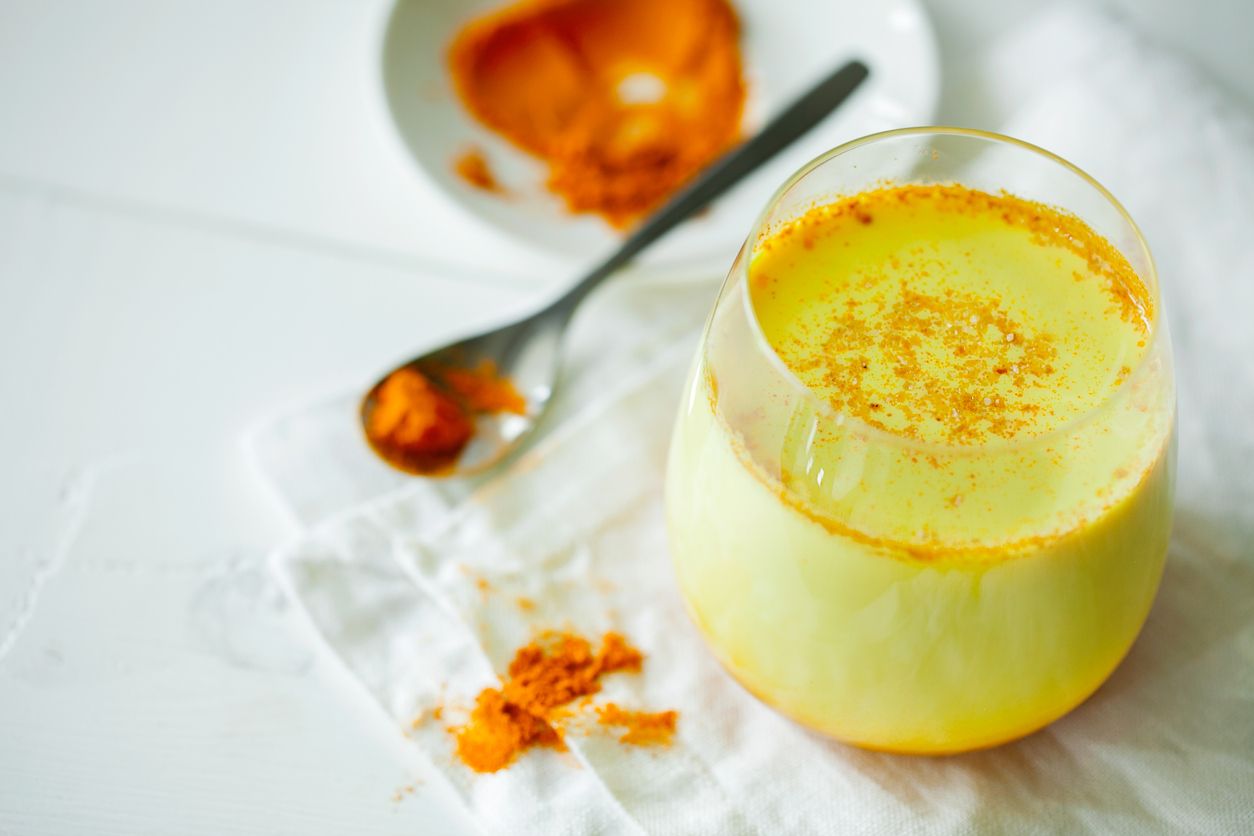Healthy ayurvedic drink golden almond milk or pumpkin turmeric latte with curcuma powder on white background close-up. Trendy Asian natural detox morning beverage with spices for vegans. Horizontal orientation