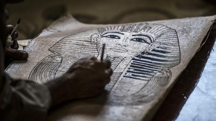 A woman cuts papyrus by a thread at the workshop in the village of al-Qaramous in Sharqiyah province, in Egypts northern fertile Nile Delta region, some kilometres northeast of the capital on July 28, 2021. - In the lush green fields of Egypts fertile Delta Valley, farmers in the small village of In the lush green fields of Egypts fertile Delta Valley, farmers in the small village of Al-Qaramus have kept alive the ancient Pharaonic tradition of making papyrus paper. In the 1970s, a plastic arts teacher taught the farmers how to reappropriate agricultural and artistic techniques dating back millenia to plant the valuable reed and transform it into brownish paper with ornate drawings and text. Al-Qaramus is now the largest hub of papyrus production nationwide, according to agricultural experts. (Photo by Khaled DESOUKI / AFP)