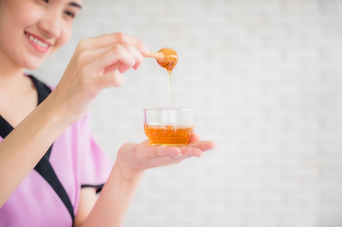 Beautiful asian young woman professional masseuse holding honey cup for spa body treatment in spa salon. Female masseuse prepared pure honey for facial mask. Beauty treatment and healthcare concept.