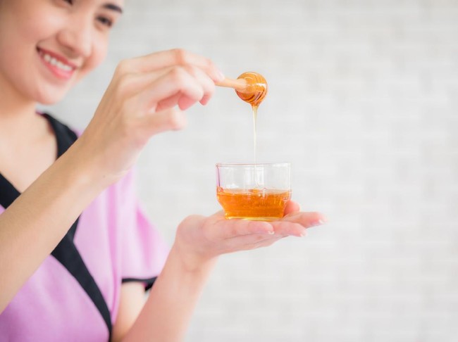 Ilustrasi madu Beautiful asian young woman professional masseuse holding honey cup for spa body treatment in spa salon. Female masseuse prepared pure honey for facial mask. Beauty treatment and healthcare concept.